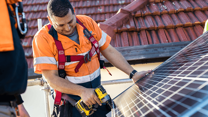 man in body harness while working on roof installing solar panels