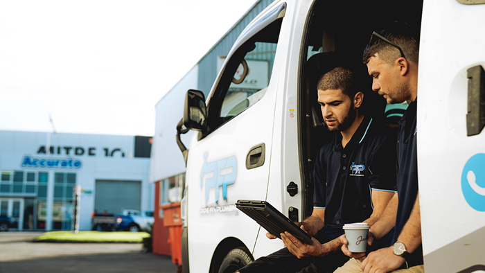 two contractors sitting on the floor of company vehicle and looking at the same device