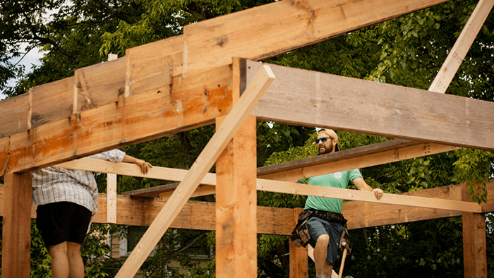 two tradies standing inside a timber house framing on ladders and looking at the roof