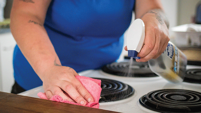 Woman cleans stovetop with cloth and bar keepers friend cleaning spray