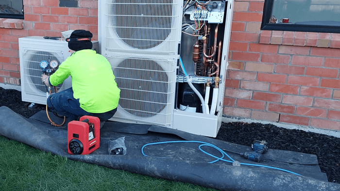 tradie working at the side of the house on HVAC pumps