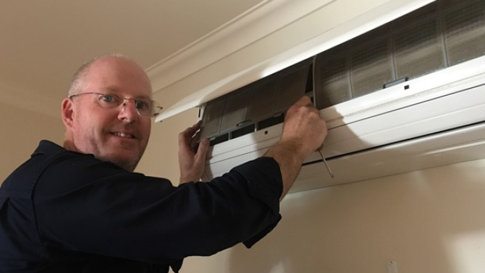 greg begelhole looking at camera while standing in-front of a wall mounted heat pump