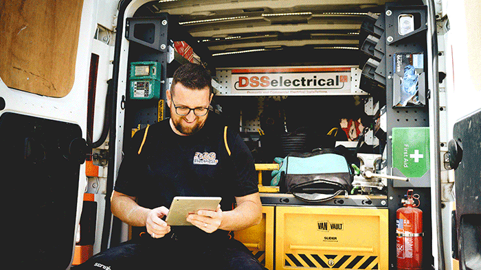 electrician sitting in back of work van looking at tablet