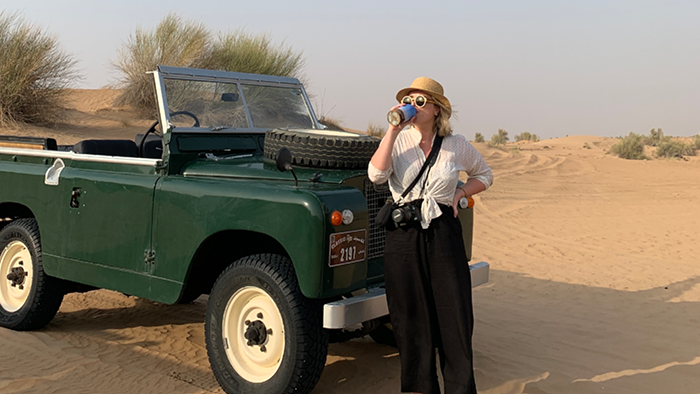 drinking from a cup next to a classic Land Rover in the desert 