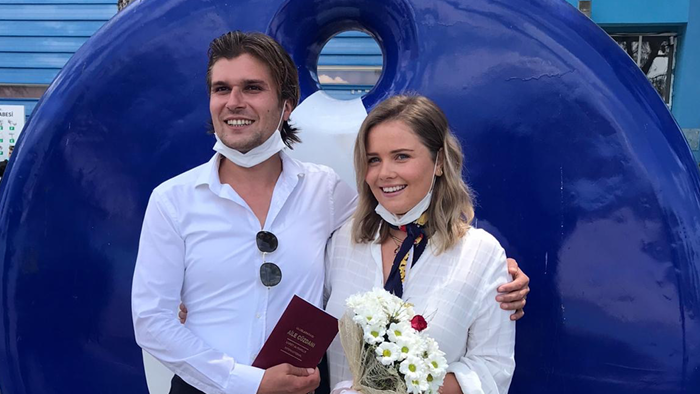 ella and her husband standing infant of a blue sculpture with flowers in hand 