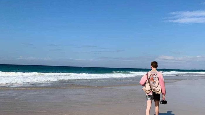sam walking on the beach with waves in the background